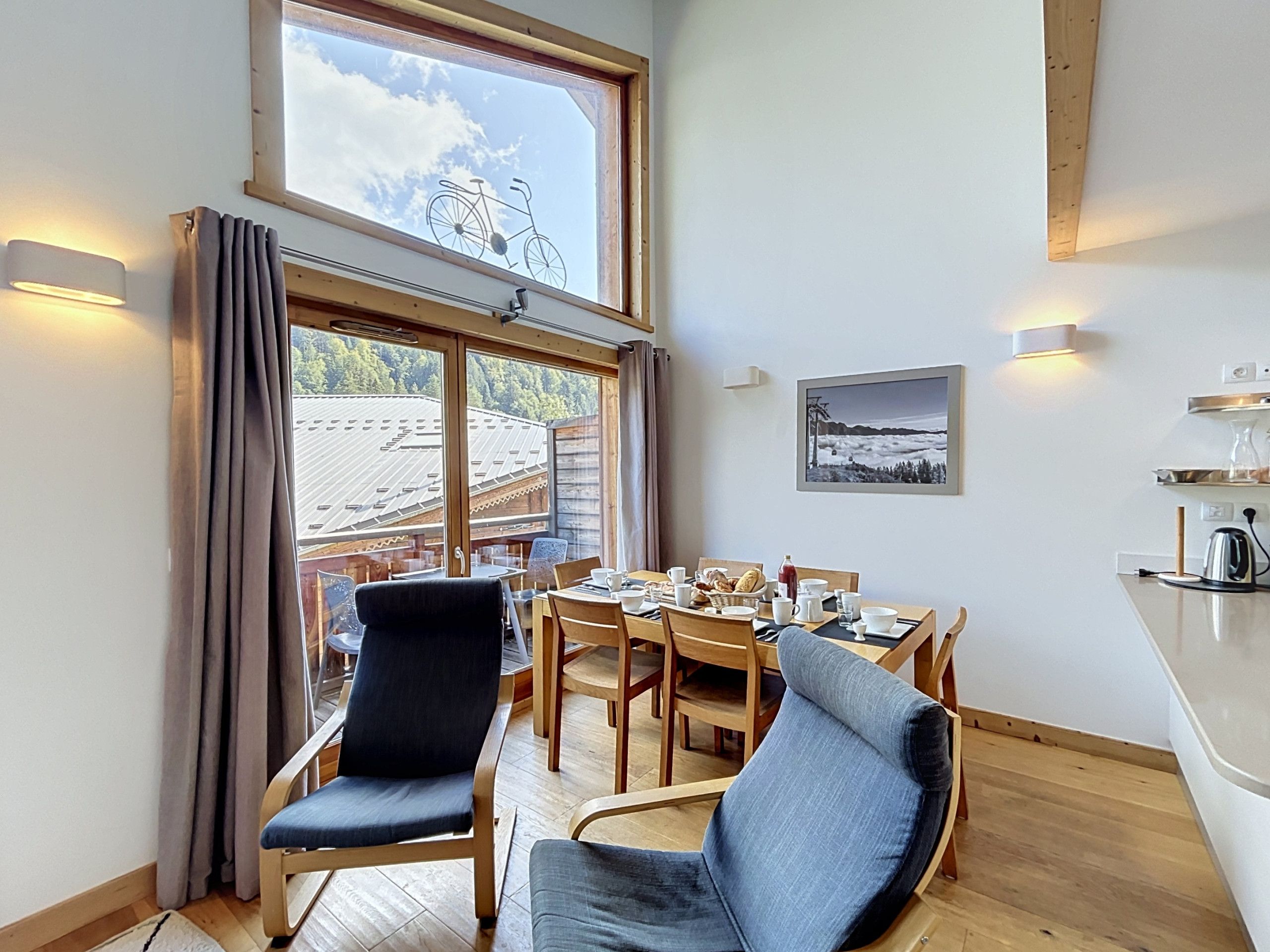 A dining area with a table set for four, chairs, a window with curtains, and a wall-mounted picture.