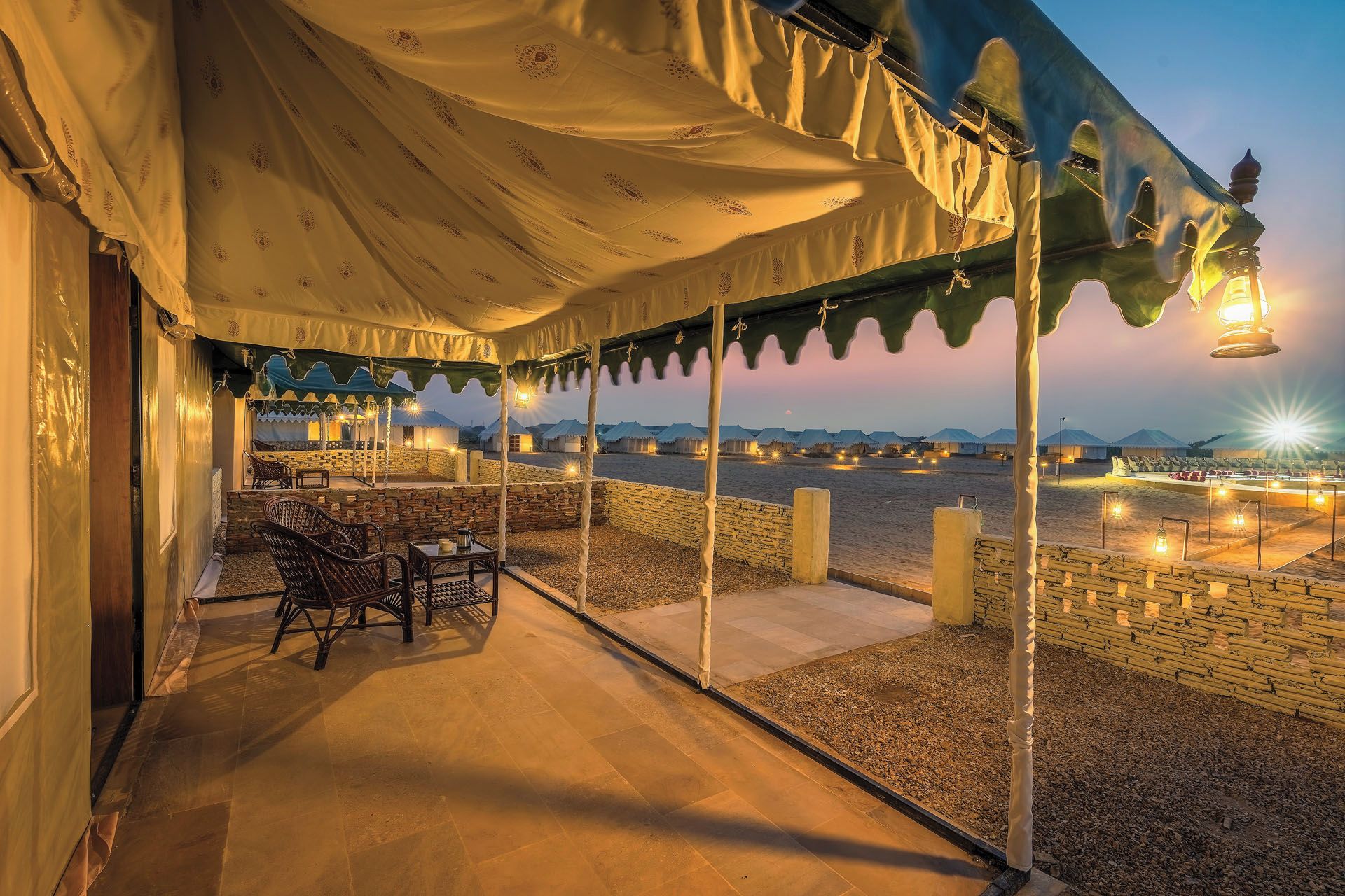 An outdoor seating area with tables and chairs, a covered patio, and a view of distant tents.