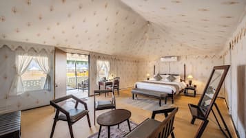 A spacious tented room with a bed, seating area, and a view of the outside.