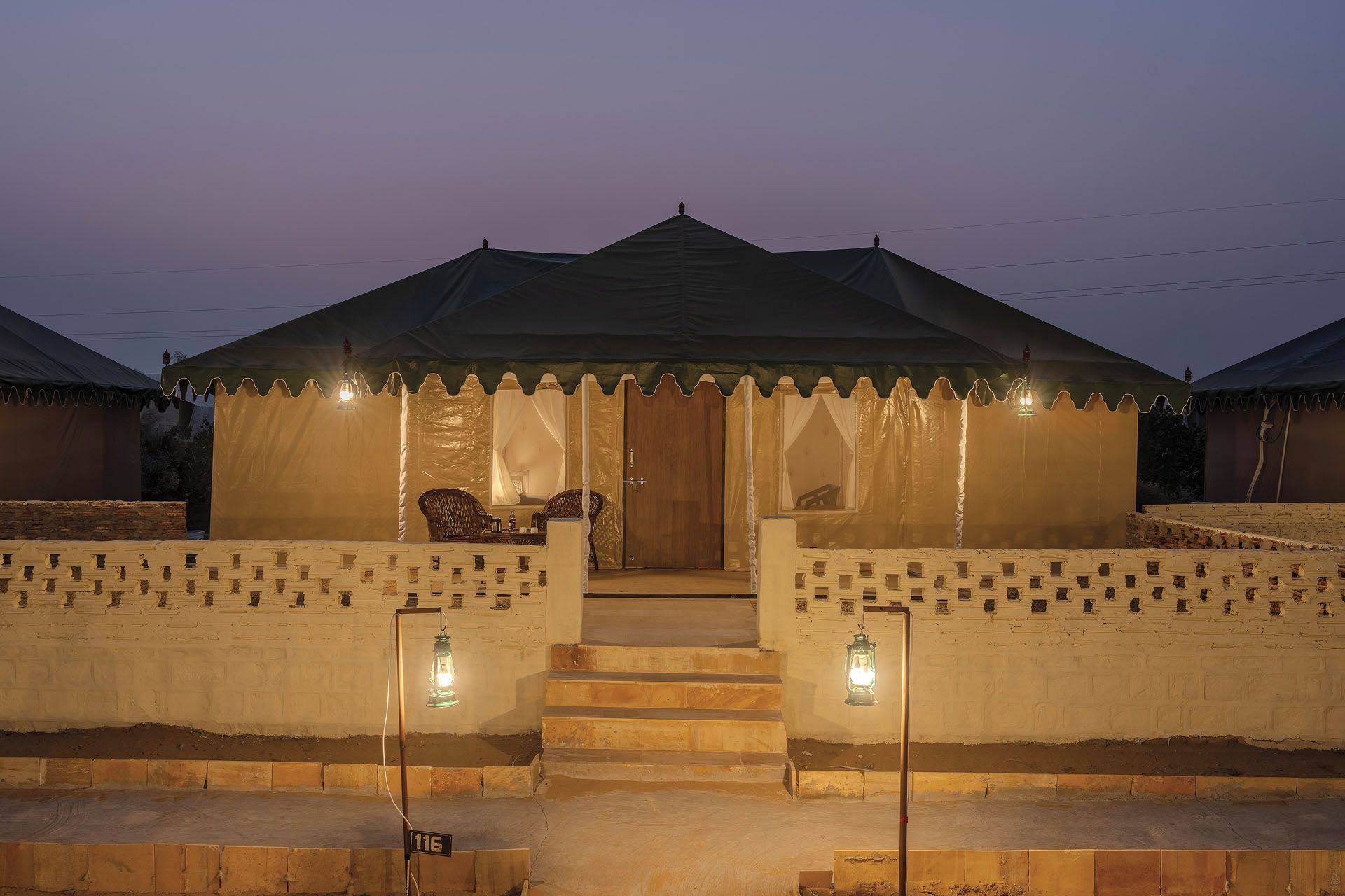 A tent-like structure with a door and steps leading up to it, surrounded by a low wall with lanterns.