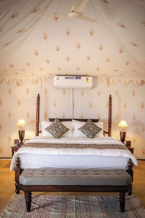 A bedroom with a four-poster bed, two bedside lamps, a ceiling fan, and a wall-mounted air conditioner. - Dangri Desert Safari Camp (Jaisalmer)