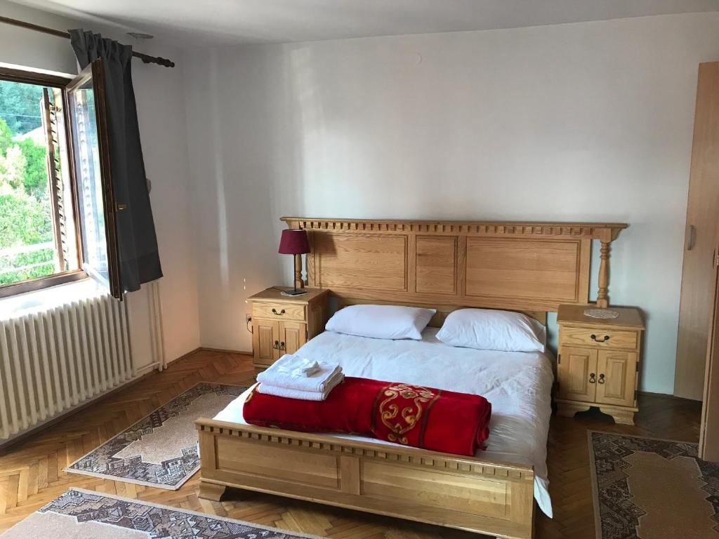 A bedroom with a wooden bed, two bedside tables, a window with curtains, and a radiator.
