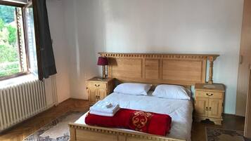 A bedroom with a wooden bed, two bedside tables, a window with curtains, and a radiator.