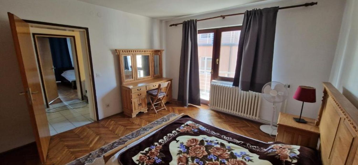 Ein Schlafzimmer mit einem Holzschrank, einem Spiegel, einer Heizung, einem Bett mit Blumenmuster und einem Fenster mit Vorhängen.