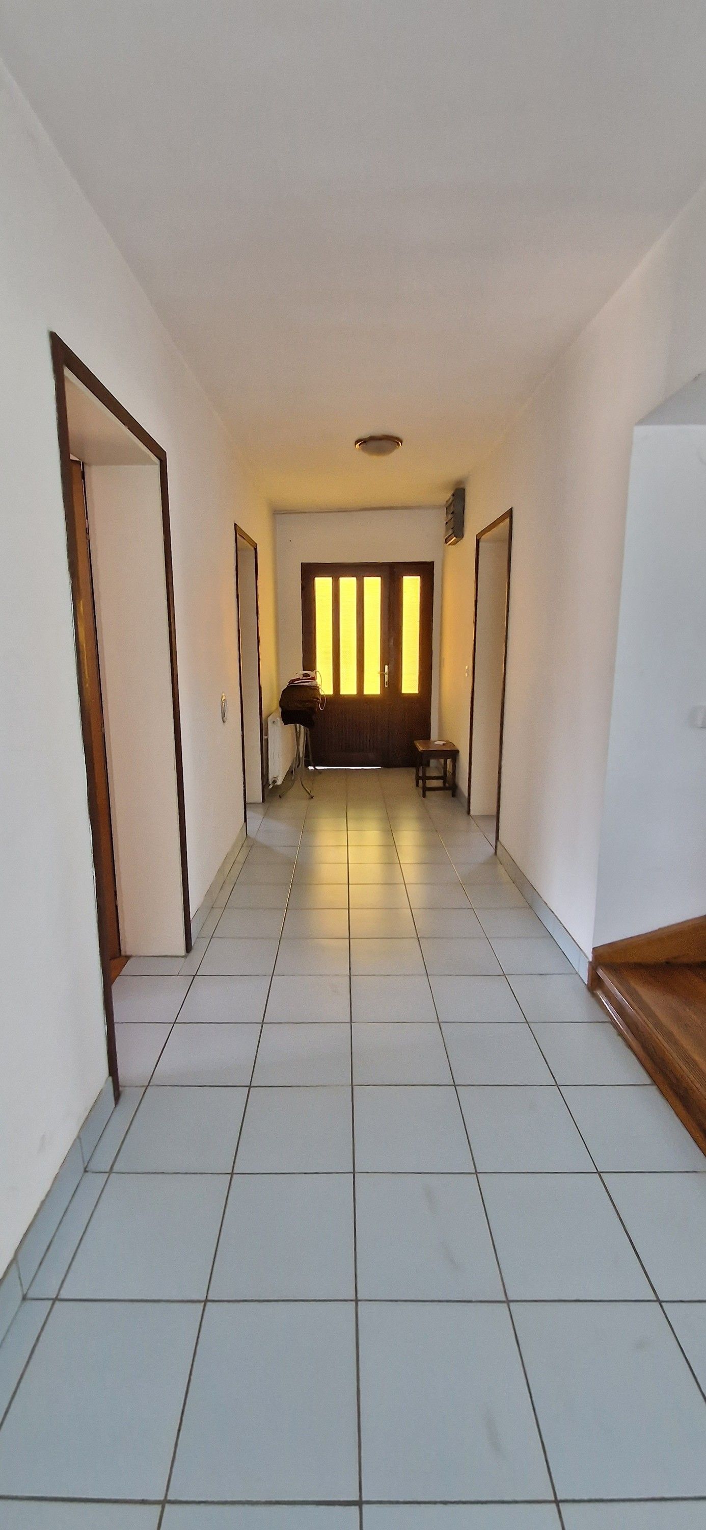 A hallway with a tiled floor, a door on the left, a bench in the center, and a door on the right.