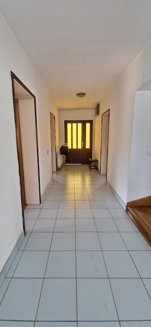 A hallway with a tiled floor, a door on the left, a bench in the center, and a door on the right.