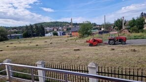 A rural landscape with a field, hay bales, a red tractor, and a distant village.
