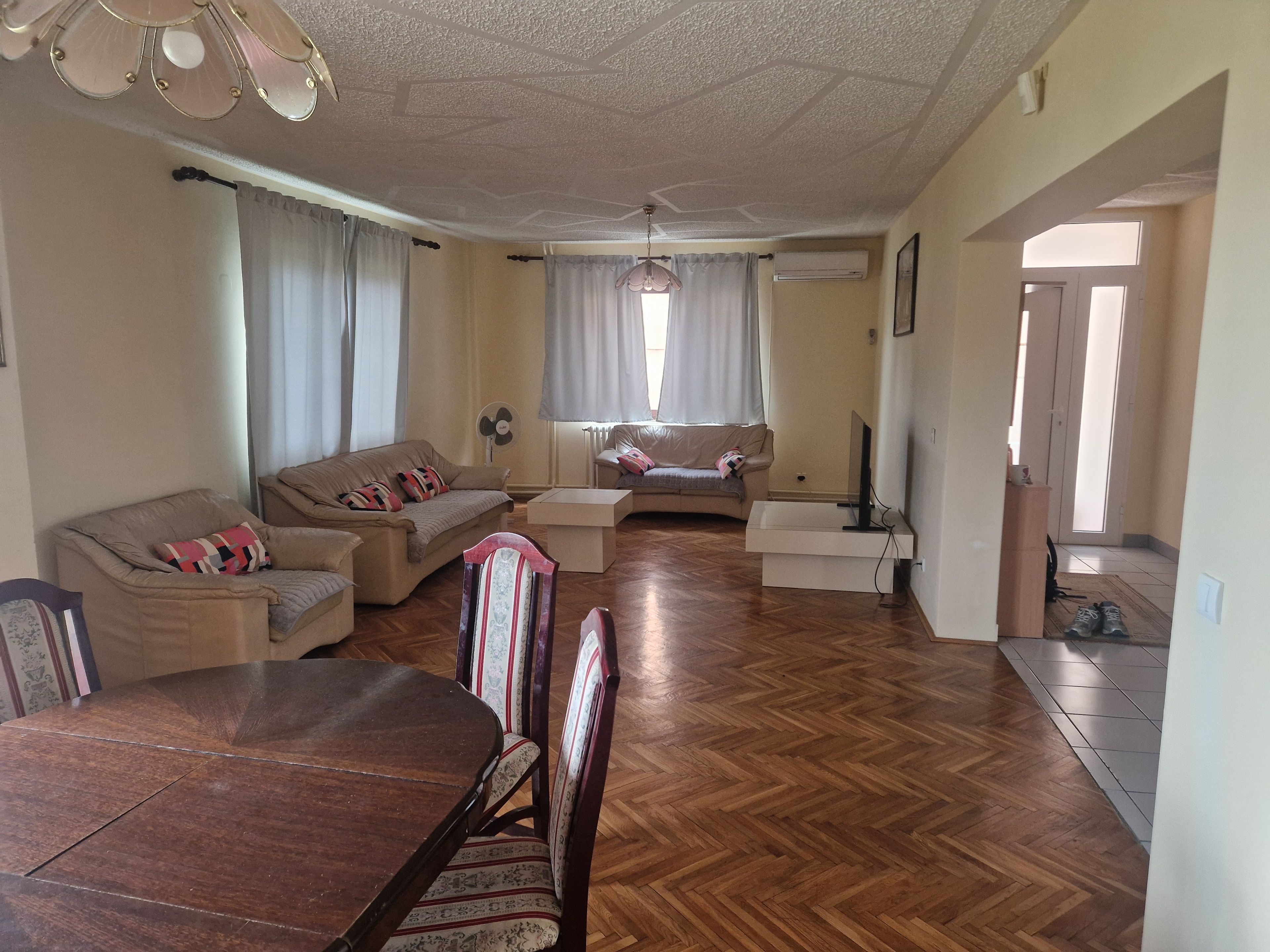 Una sala de estar con piso de madera, dos sofás, una mesa de comedor con sillas y un televisor.