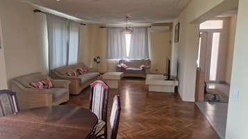 Una sala de estar con piso de madera, dos sofás, una mesa de comedor con sillas y un televisor.