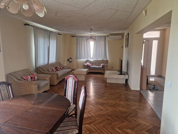 A living room with a wooden floor, two sofas, a dining table with chairs, and a television.