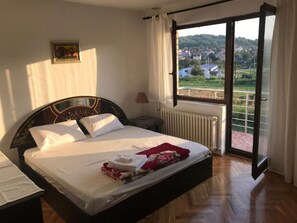 Ein Schlafzimmer mit Bett, Nachttisch, Fenster mit Blick auf eine Stadt und Heizkörper.