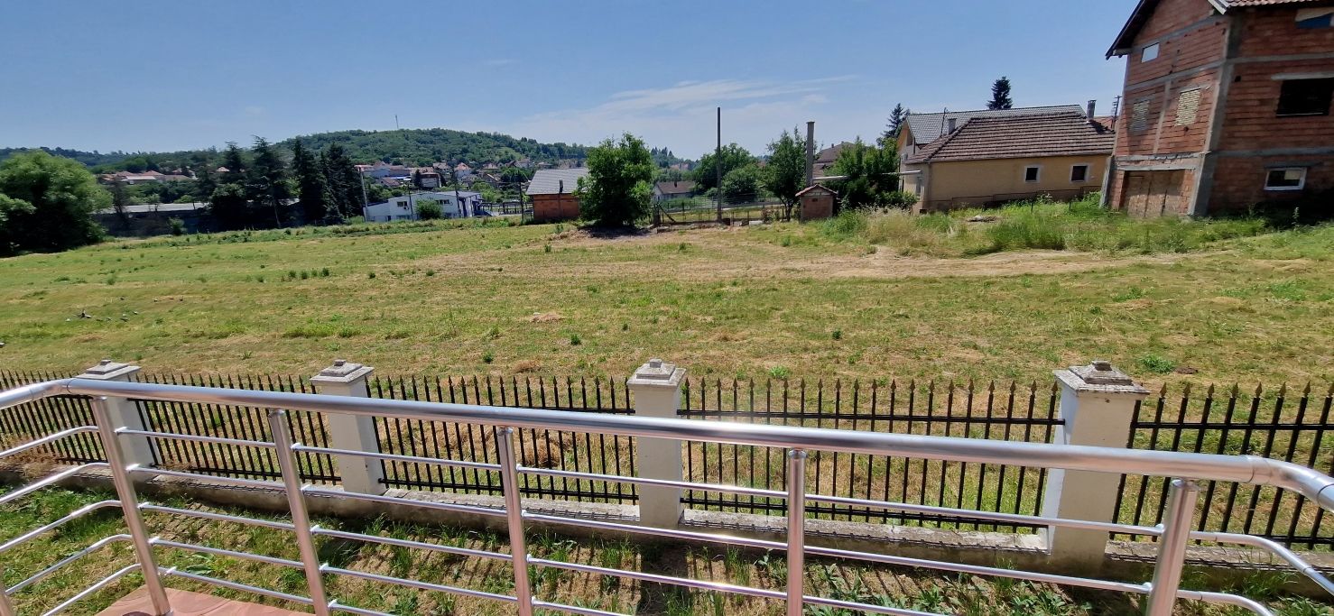 Ein eingezäunter Außenbereich mit einer grünen Wiese, einem Gebäude mit rotem Dach und blauem Himmel.