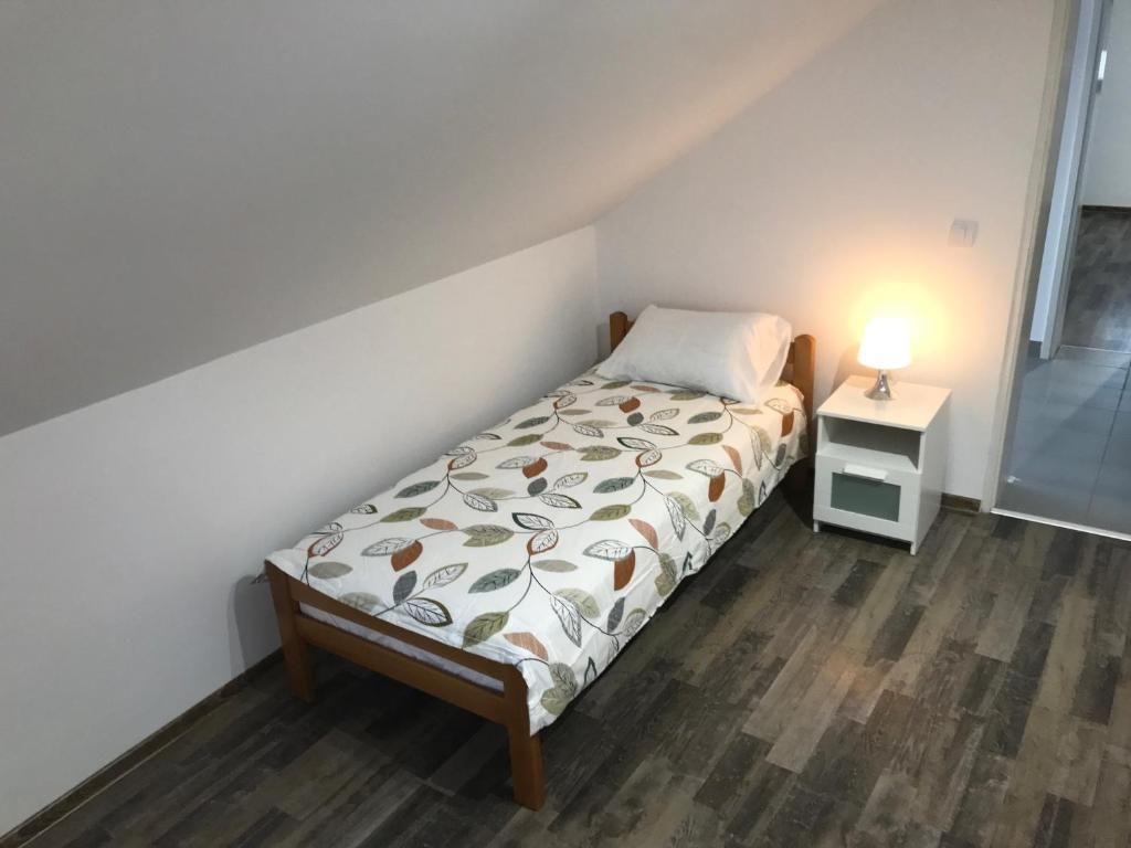 Habitació petita amb un llit individual de fusta, un edredó estampat, una taula de nit amb una làmpada i vista a un passadís.