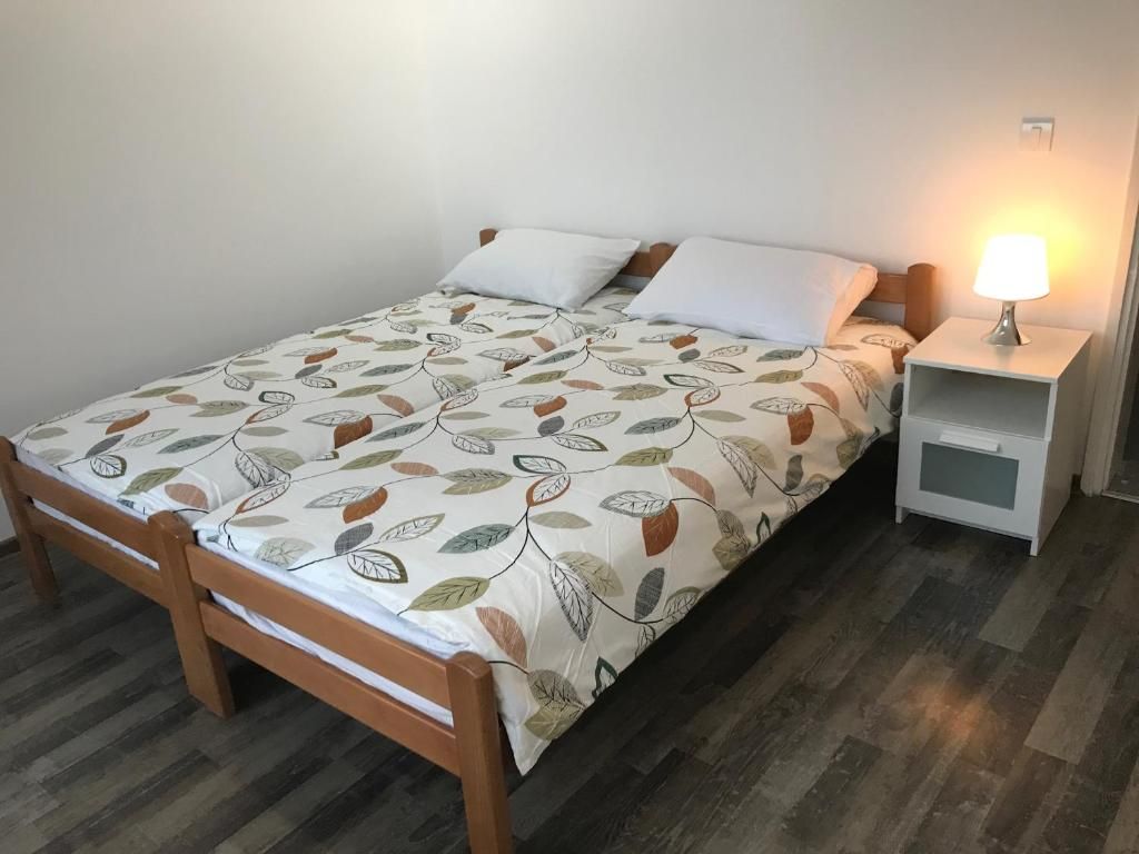 Ein Einzelbett mit einem blattgemusterten Überwurf, ein Nachttisch mit einer Lampe und ein weiterer Nachttisch.