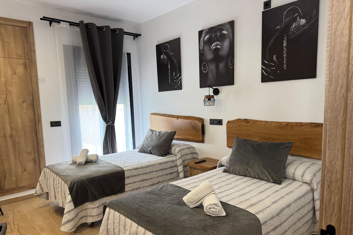 Habitación de hotel con dos camas, cabecera de madera, mesita de noche, lámpara de pared y una obra de arte.