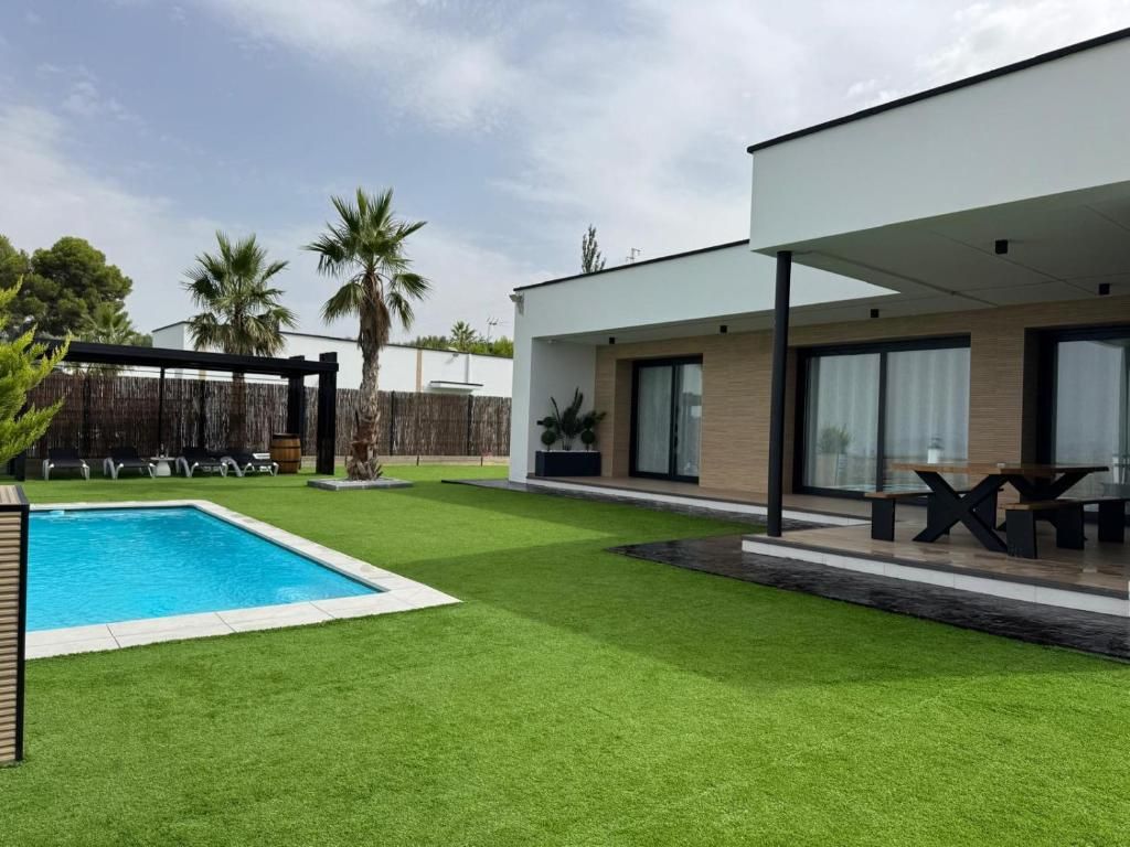 Una casa moderna con piscina, un patio cubierto y un césped bien cuidado.