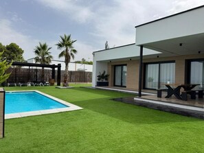 A modern house with a swimming pool, a covered patio, and a well-maintained lawn.