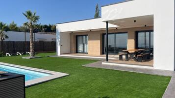 A modern house with a swimming pool, a patio with outdoor furniture, and a well-maintained lawn.