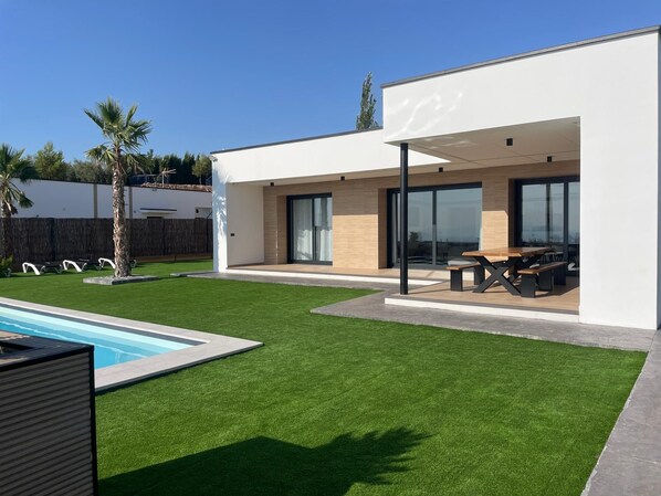 A modern house with a swimming pool, a patio with outdoor furniture, and a well-maintained lawn.