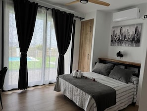 Een slaapkamer met een bed, een plafondventilator, een schilderij en uitzicht op de omgeving.