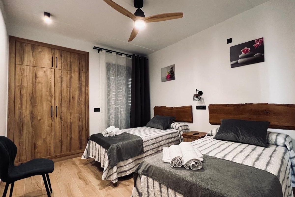Een kamer met twee bedden, een houten kledingkast, een plafondventilator en een klein tafeltje.