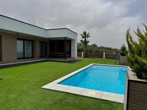 A modern house with a swimming pool, a covered patio, and a well-maintained lawn.