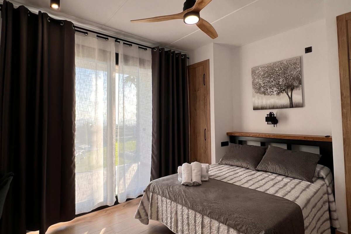A bedroom with a bed, a ceiling fan, a painting, and a window with curtains.