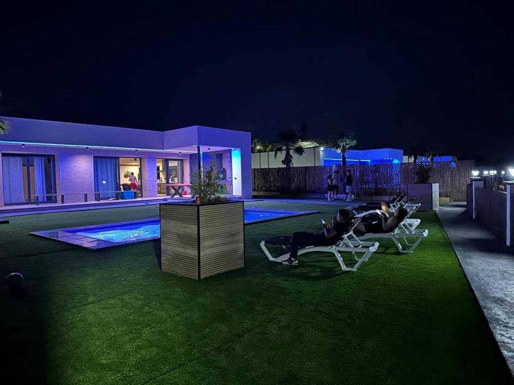 Zona exterior moderna amb piscina, gandules i un edifici amb finestres il·luminades.