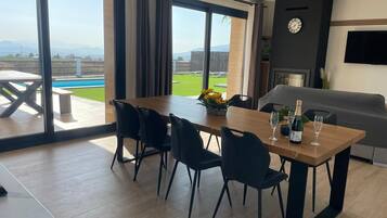 Un comedor moderno con una mesa de madera, sillas negras y vistas a una piscina y montañas.