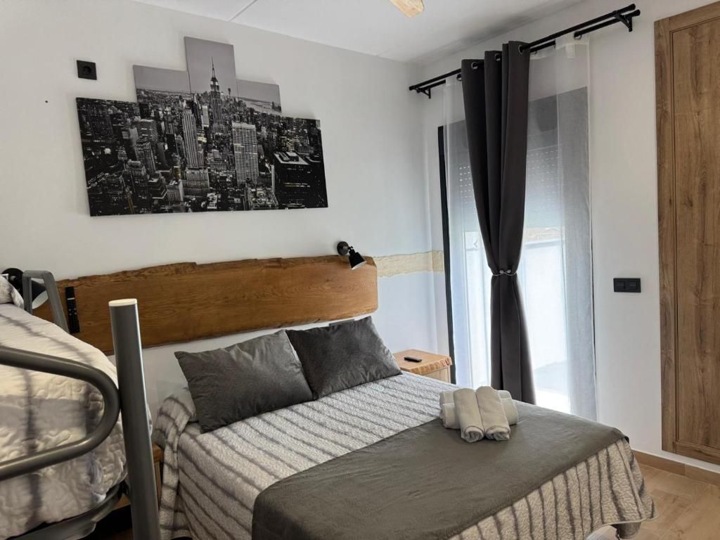 Un dormitorio con una cama, un cabecero, una pintura de paisaje urbano, una ventana con cortinas y un armario de madera.