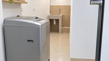 A compact, modern laundry room with a front-loading washing machine, a sink, and a towel rack.