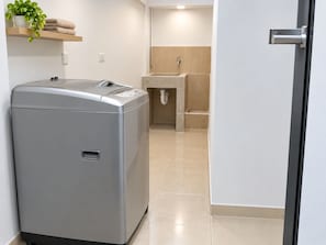 A compact, modern laundry room with a front-loading washing machine, a sink, and a towel rack. - Apto duplex con vista a la calle (Medellin)