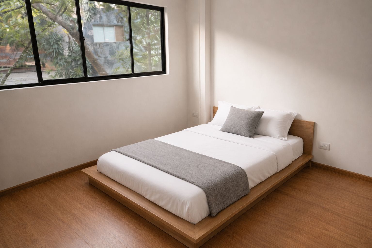 A single bed with a wooden frame, white bedding, and a grey throw blanket.