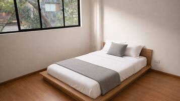 A single bed with a wooden frame, white bedding, and a grey throw blanket.
