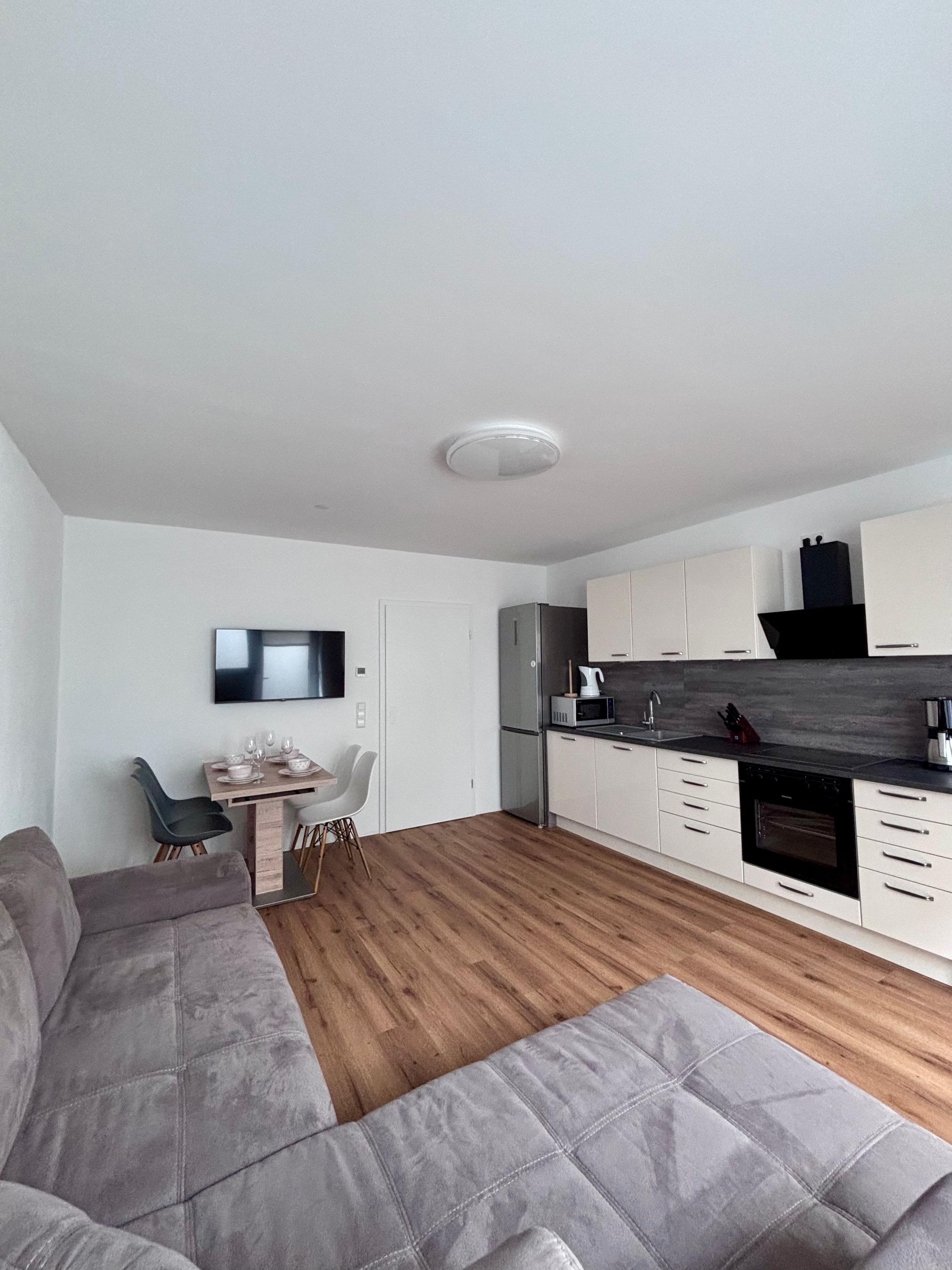 A modern kitchen with white cabinets, a built-in oven, and a dining area with a table and chairs.