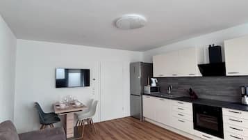 A modern kitchen with white cabinets, a built-in oven, and a dining area with a table and chairs.