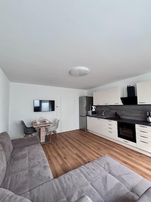A modern kitchen with white cabinets, a built-in oven, and a dining area with a table and chairs.