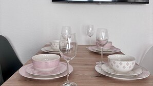 Een eettafel met roze en witte borden en wijnglazen, een flatscreen televisie aan de muur en een houten tafelblad.