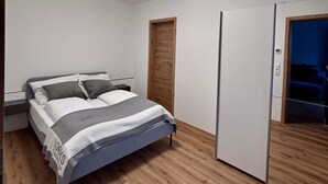 Een slaapkamer met een bed, houten vloeren, een garderobe en een deur.