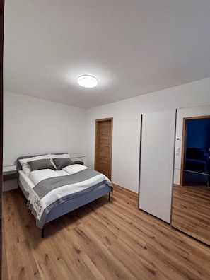 Ein Schlafzimmer mit einem Bett, Holzboden, einem Kleiderschrank und einer Tür.