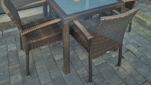 Een terras met een glazen tafel, rieten stoelen, een lamp en een pompoen decoratie.
