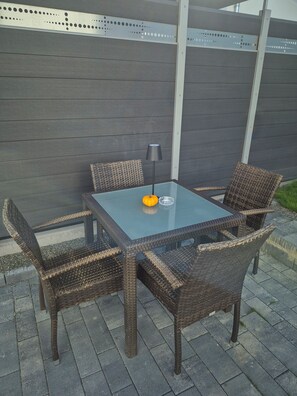 Eine Terrasse mit einem Glastisch, Korbstühlen, einer Lampe und einer Kürbisdekoration.