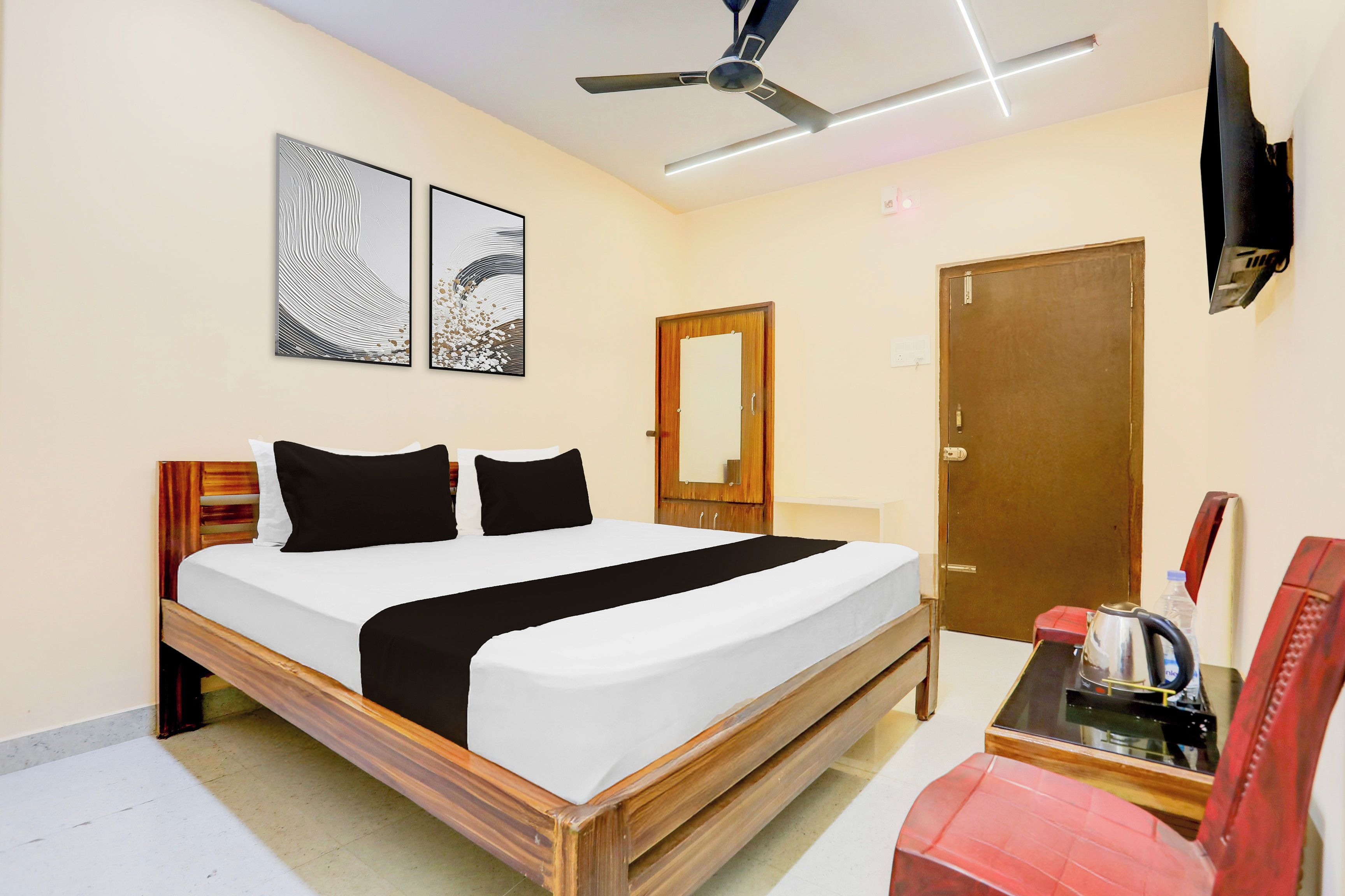 A hotel room with a bed, a ceiling fan, a door, and a television mounted on the wall.