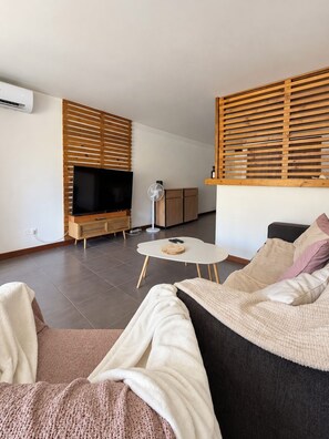 A modern living room with a flat-screen TV, wooden slatted wall, a round coffee table, and a sofa with a throw blanket. - A tropical retreat under the Saint Martin sun (Cul-de-Sac)