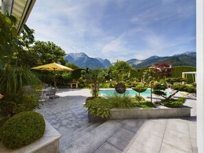 A pool area with a mountain backdrop, surrounded by well-maintained gardens and outdoor furniture.