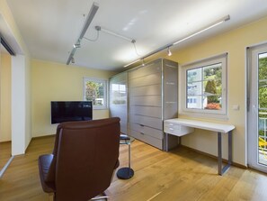 A modern room with a wooden floor, a brown leather chair, a TV, a sliding door closet, and a window with a view.