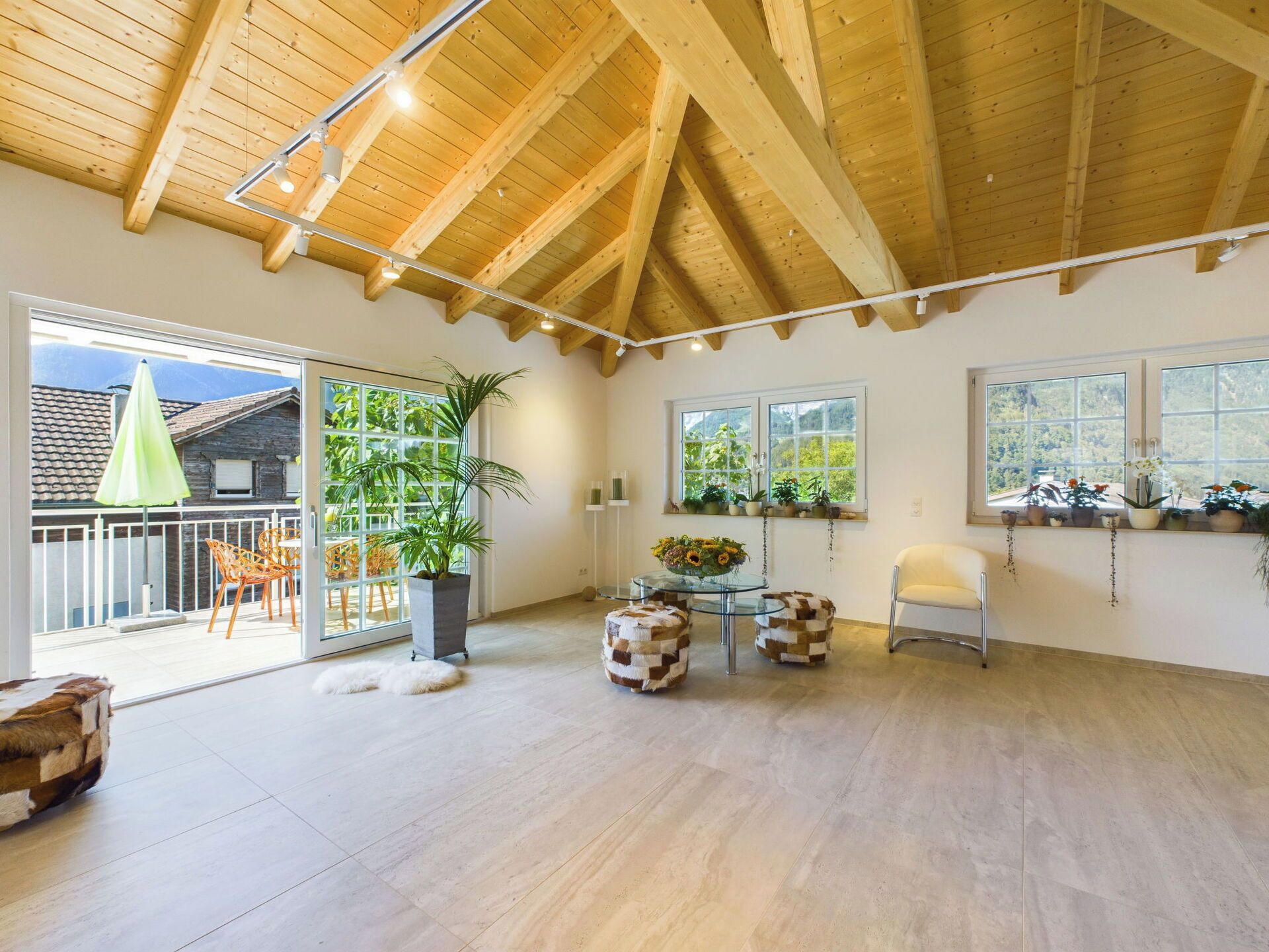 Une pièce spacieuse avec un haut plafond en bois, de grandes fenêtres et un balcon aménagé avec du mobilier d’extérieur.