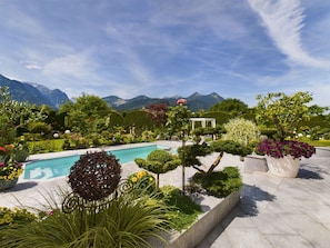 A landscaped garden with a swimming pool, manicured hedges, and a view of mountains.
