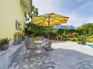 An outdoor patio with a table and chairs, surrounded by potted plants and a large umbrella.