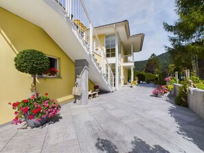 A two-story building with a staircase leading to a balcony, surrounded by potted plants and flowers.